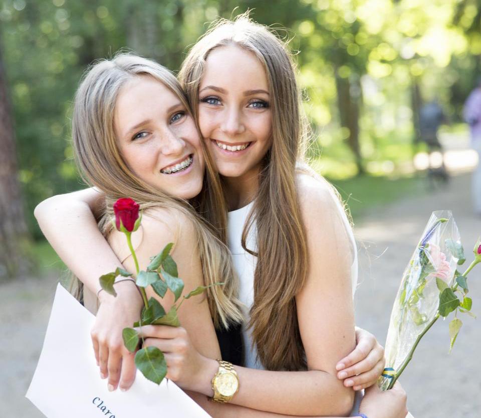 To jenter som klemmer med rose og vitnemål i hendene.