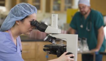 Kvinnelig biolog ser i et mikroskop.